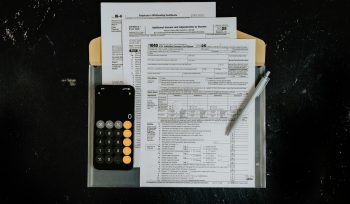 Tax forms with calculator and pen on dark surface