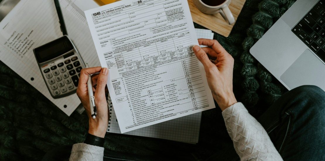 Hands holding tax forms with calculator and laptop.