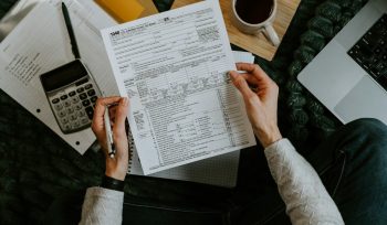 Hands holding tax forms with calculator and laptop.