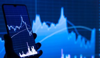 Navigating market volatility with passive income concept showing a smartphone displaying financial market charts against a blue investment graph background.