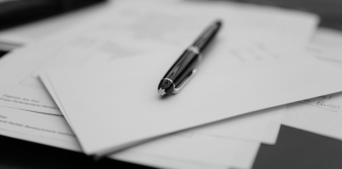 A pen sitting on top of a pile of papers. When should you update your will? A 2026 will beside an older 2010 will on a navy leather desk.
