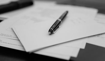A pen sitting on top of a pile of papers. When should you update your will? A 2026 will beside an older 2010 will on a navy leather desk.