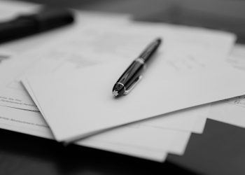 A pen sitting on top of a pile of papers. When should you update your will? A 2026 will beside an older 2010 will on a navy leather desk.