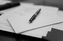 A pen sitting on top of a pile of papers. When should you update your will? A 2026 will beside an older 2010 will on a navy leather desk.